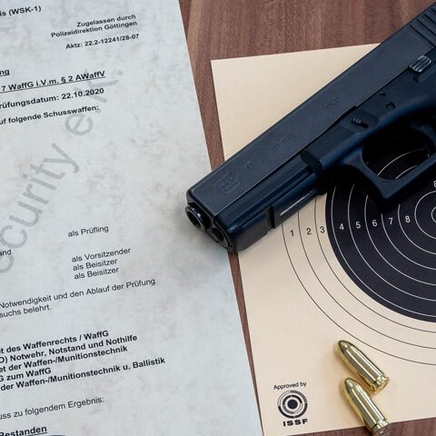 Handfeuerwaffe neben einem Zielblatt und Sicherheitsdokumenten auf einem Tisch.